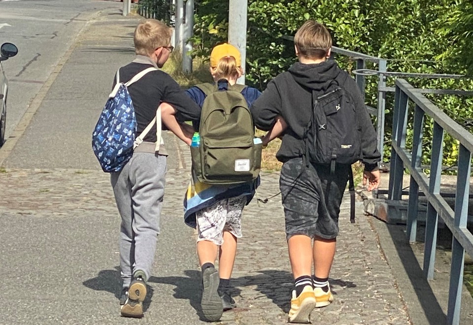 To drenge holder at tredje dreng under armen og støtter ham, mens de går langs en vej