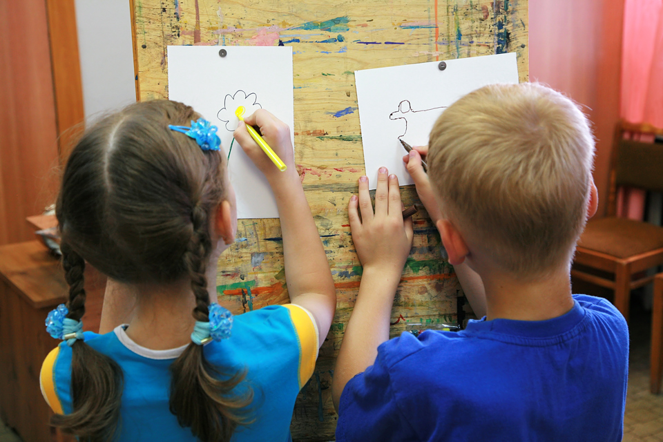 en dreng og en pige står med ryggen til beskueren og tegner